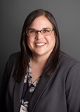 headshot of a smiling woman with shoulder-length dark hair in a charcoal grey suit